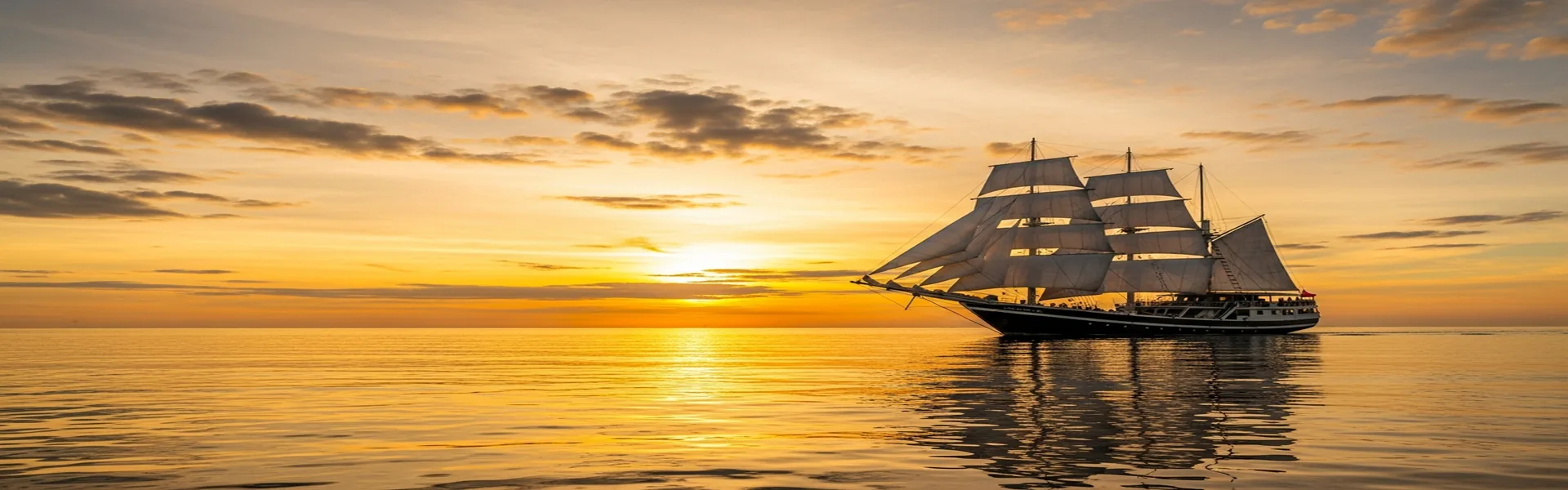 Phinisi sailing boat with white sails against sunset
